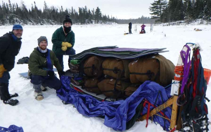 a group of gap year students pack a dog sled on a frozen snowy lake
